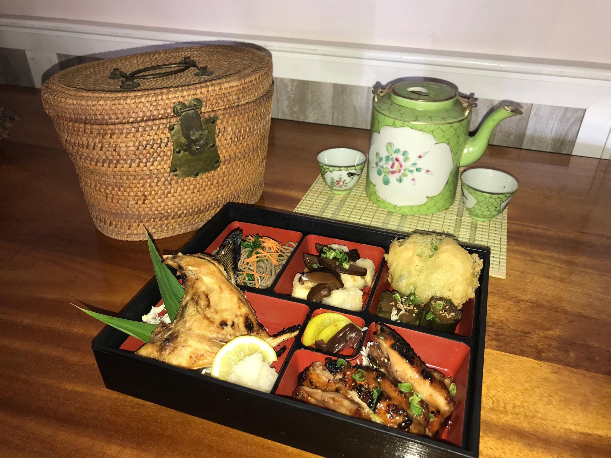 A Natsunoya bento in a lacquered box beside a green porcelain teapot and cups on a wooden table