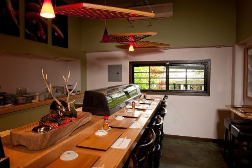 The sushi bar at Natsunoya: a wooden counter with stools, the sushi case, and a window onto the trees