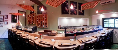 The sushi bar at Natsunoya: a curved wooden counter with stools, the sushi case, and red pendant lamps