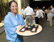 A server in a blue kimono carrying a tray of sushi to guests at a party